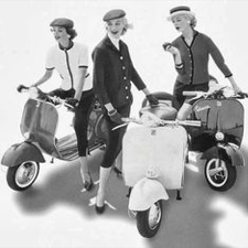 Black and white vintage photo of women standing beside Vespas.